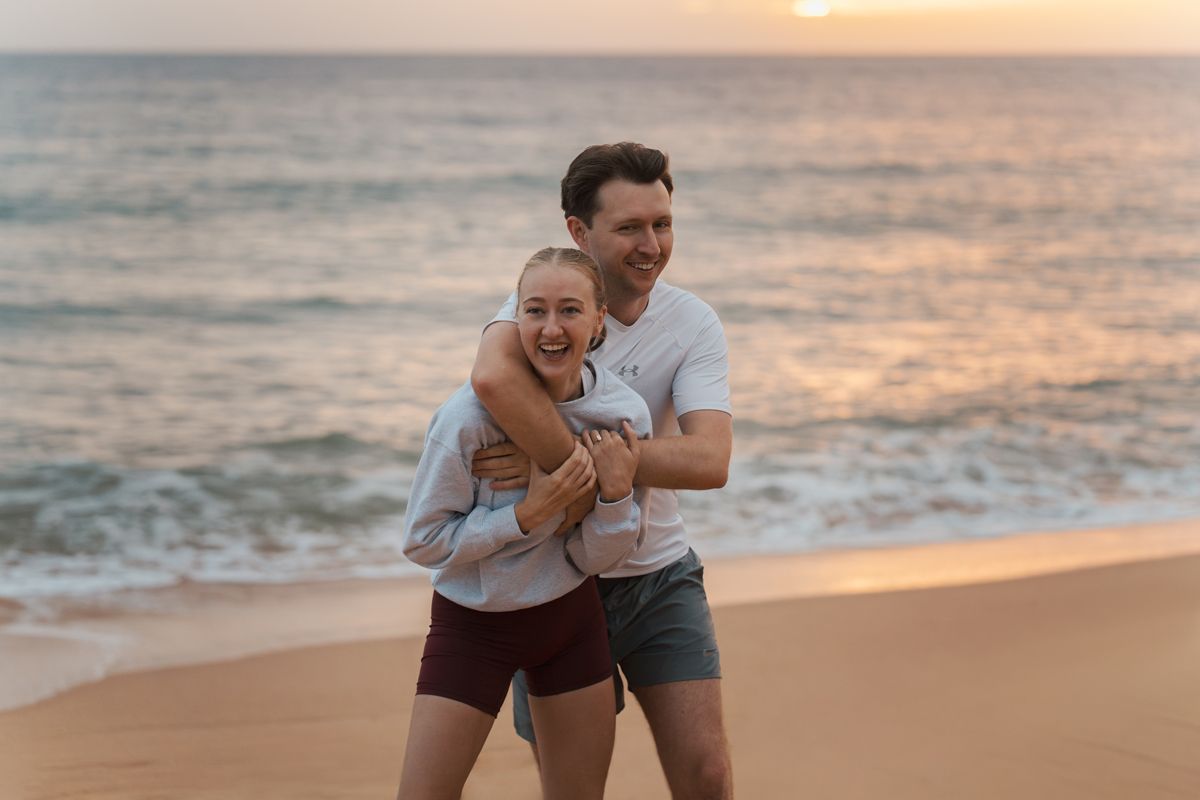 A couple shares a romantic moment on the beach at sunrise, laughing together by the ocean at Newport Beach Sydney engagement photoshoot