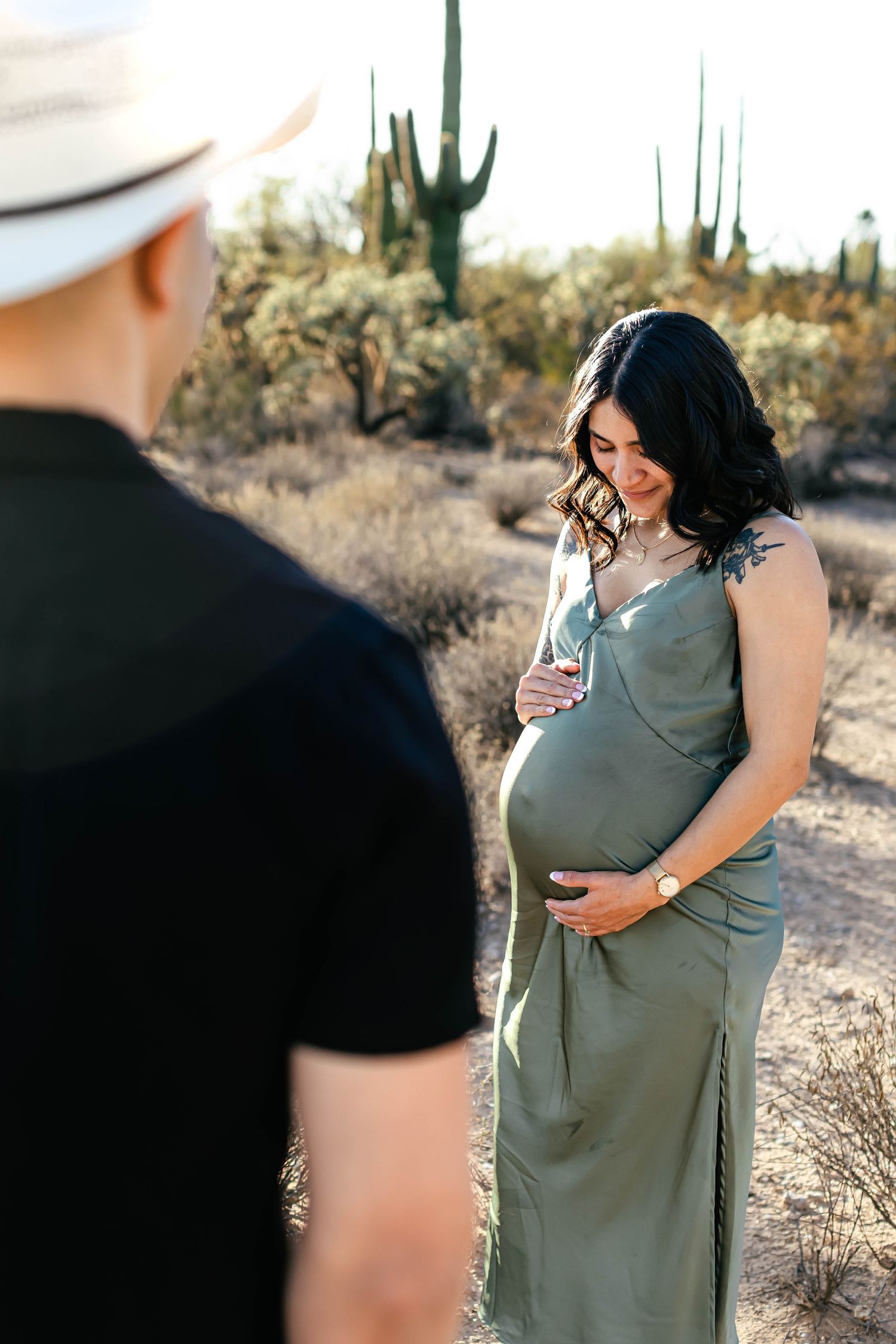 Desert maternity photoshoot among saguaro cacti during golden hour.
