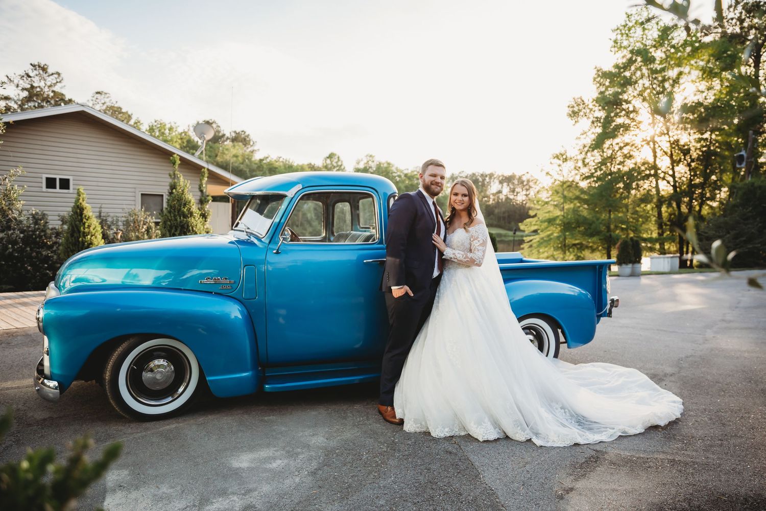 A classic blue vintage car parked outdoors serves as a backdrop for wedding photos at sunset.