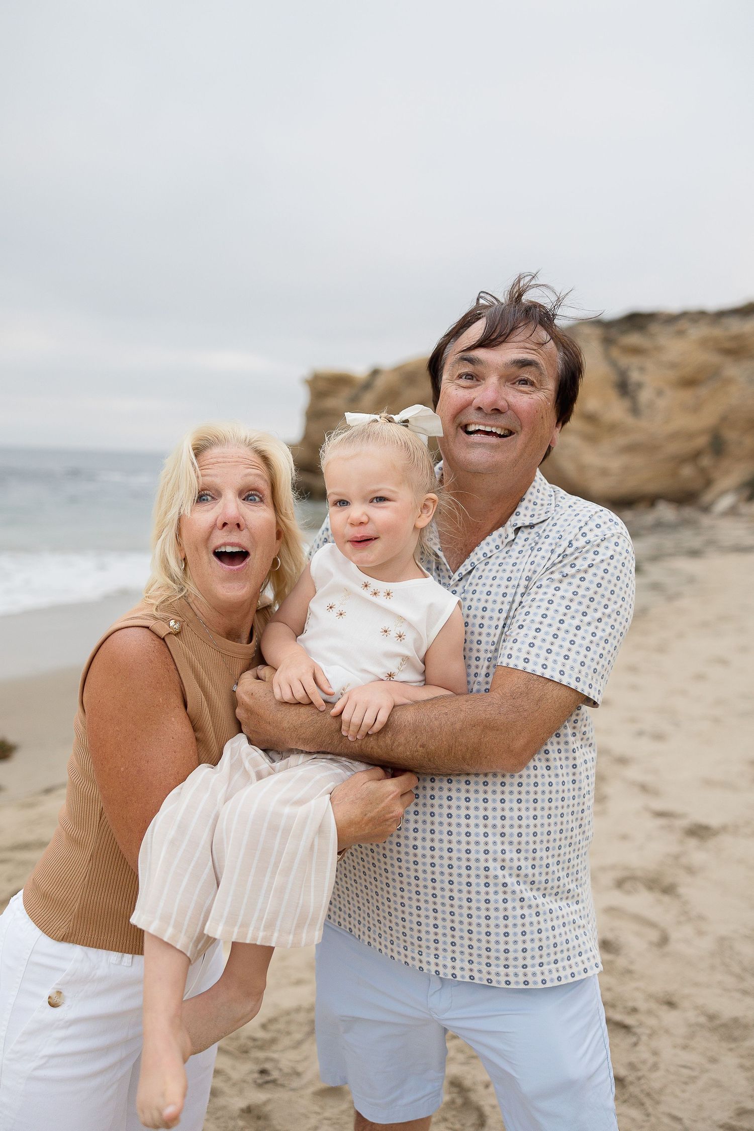 A family shares joyful moments together on a sandy beach with cliffs and ocean in the background.