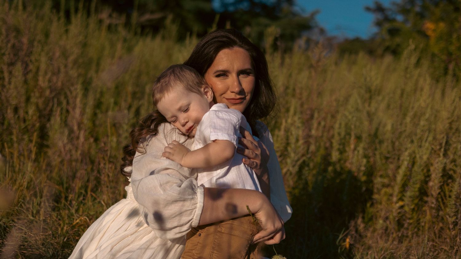 A series of outdoor family portraits taken in a golden field during sunset showing tender embraces and candid moments.