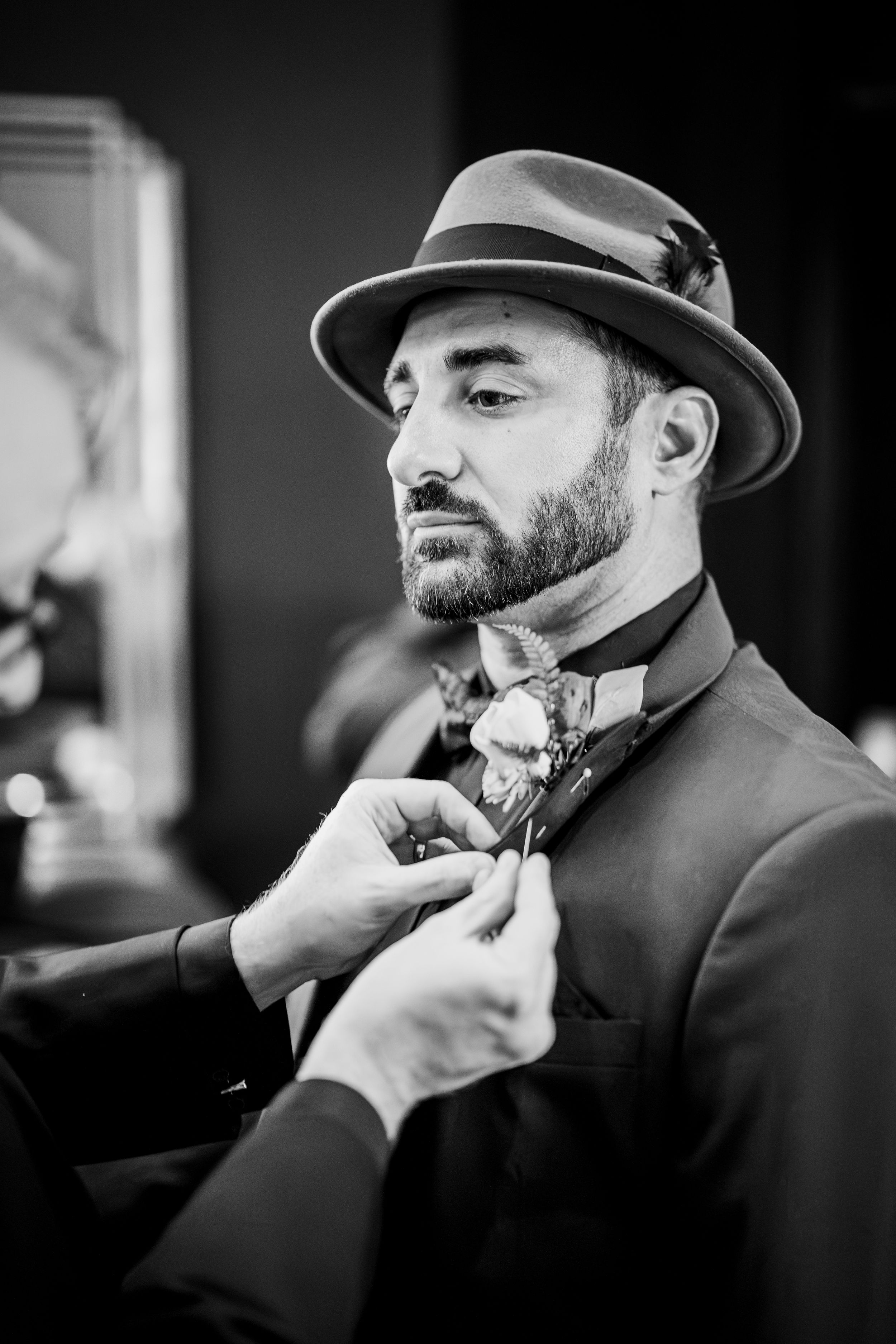 Black and white series showing a bearded man in a hat getting his beard trimmed at a barbershop.