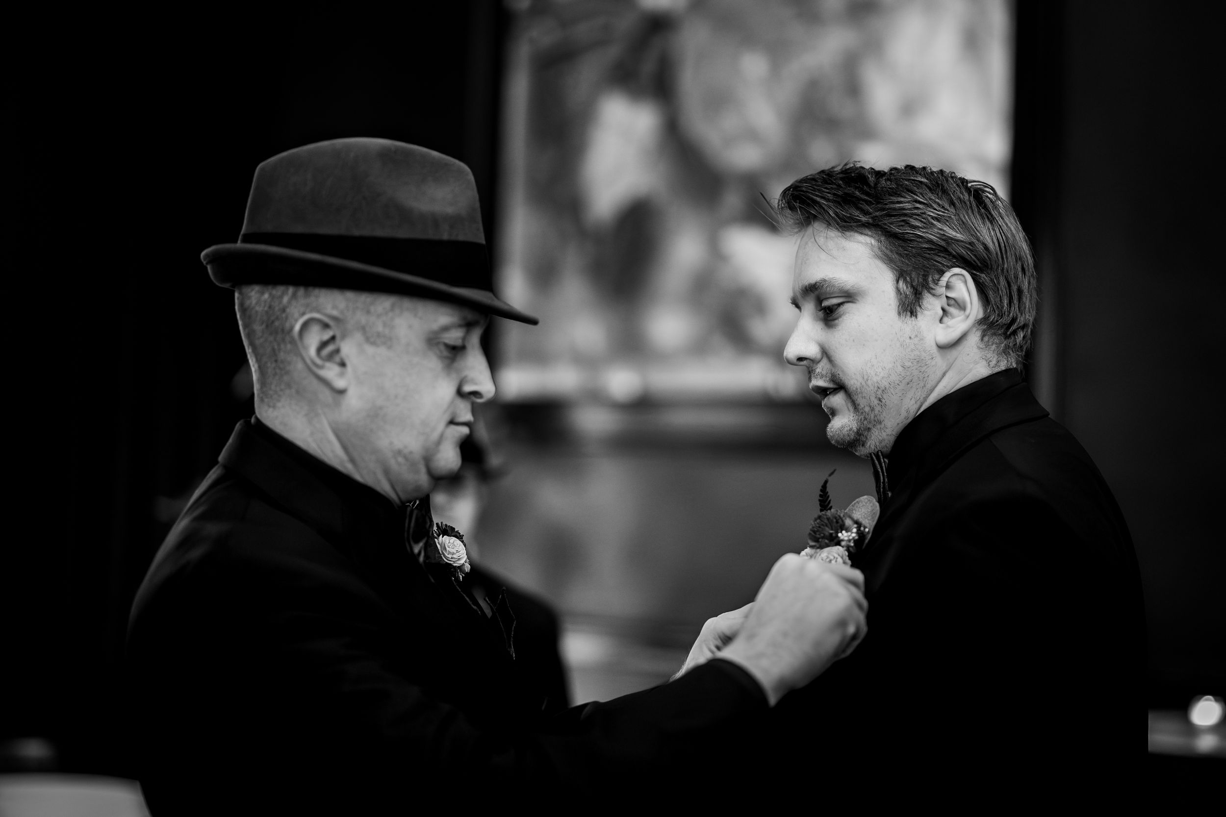 Two people in dark coats and hats have a conversation in a black and white film noir style photograph.