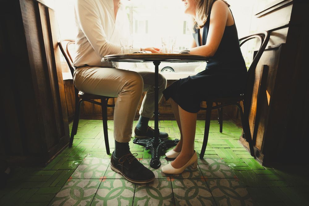 Candid detail photo of Hannah and Connor’s legs and shoes under the table at La Bonne Vache, highlighting a relaxed date-style moment during