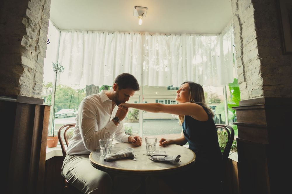 Two people share a romantic moment while dining together at a cozy window-side table in a restaurant.