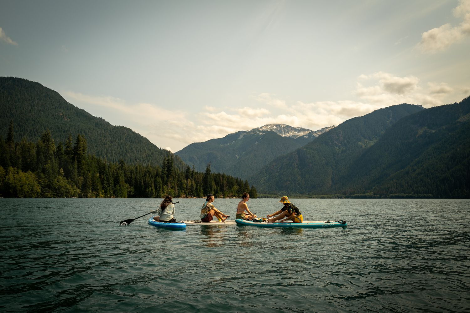 Four people paddleboarding on a serene mountain lake with forested peaks in the background.
