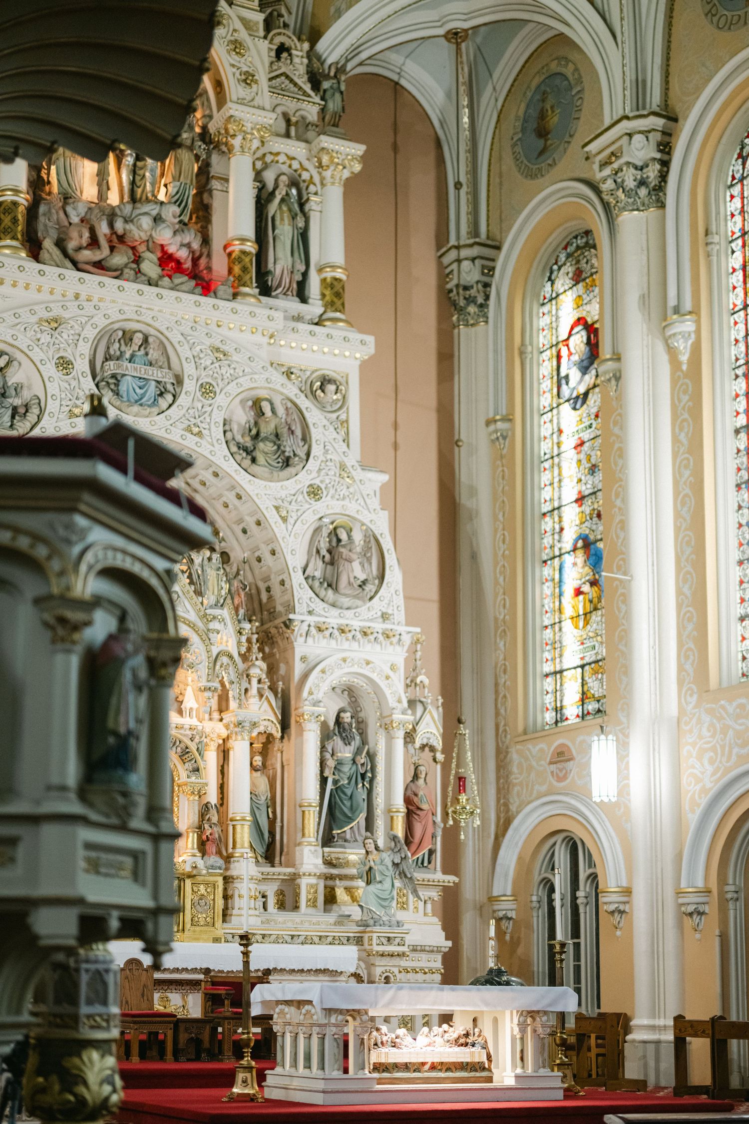 Interior view of an ornate Catholic church altar with white baroque architecture and stained glass windows.