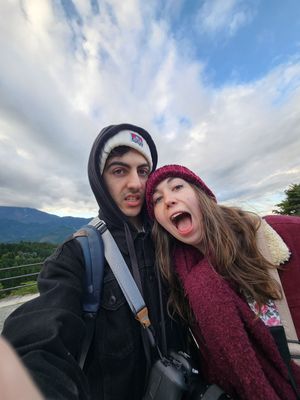 A couple sharing playful moments outdoors on a cloudy day with mountains in the background.