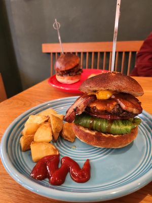 Delicious hamburgers served on blue plates with potato wedges and cherry tomatoes on a wooden table.