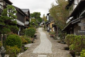 A traditional Japanese stone-paved street lined with historic wooden buildings and lush greenery in Magome post town.