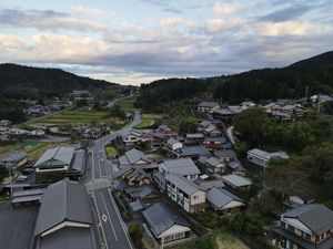 Aerial view of a small rural Japanese town nestled in mountains with traditional houses and buildings at dusk.
