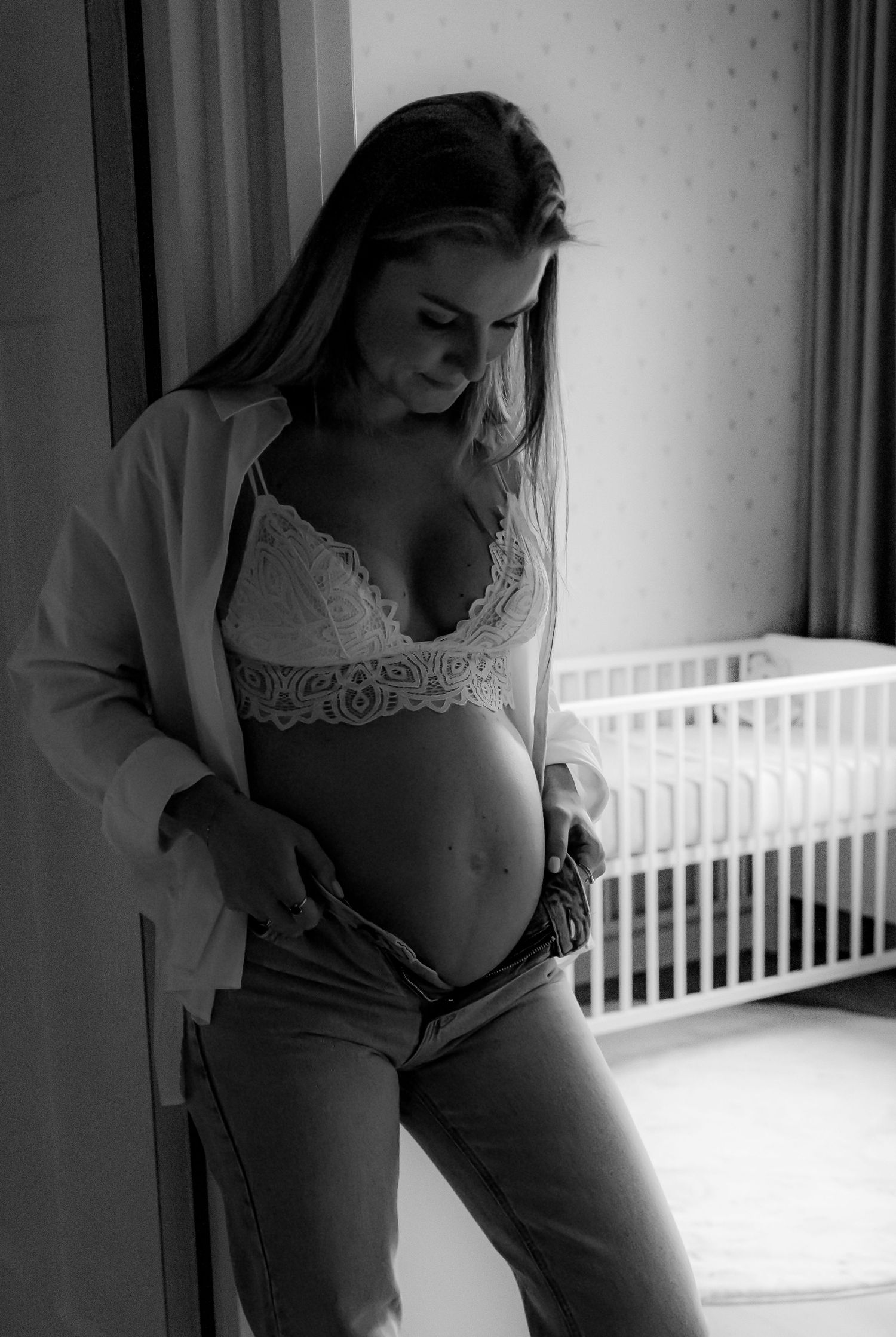 Artistic black and white maternity photos in a nursery with natural window light.