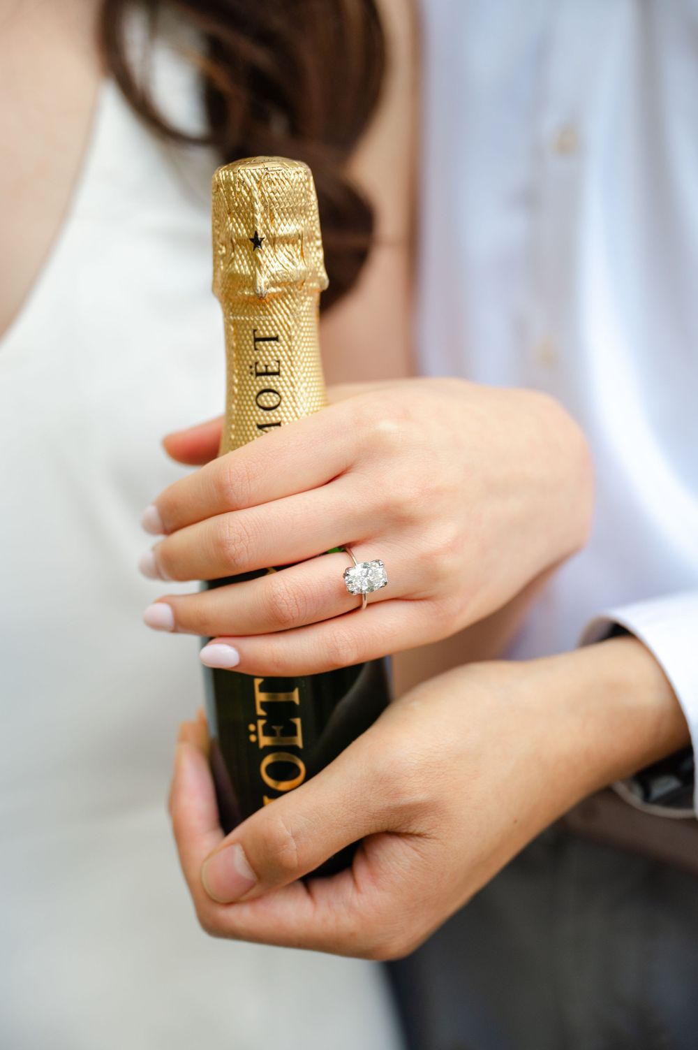 Close-up of hands holding a champagne bottle showing an engagement ring.