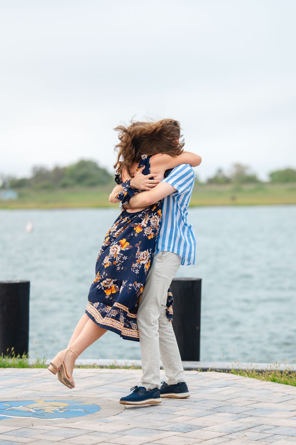 A couple embraces in a romantic moment by the waterfront on a paved walkway.