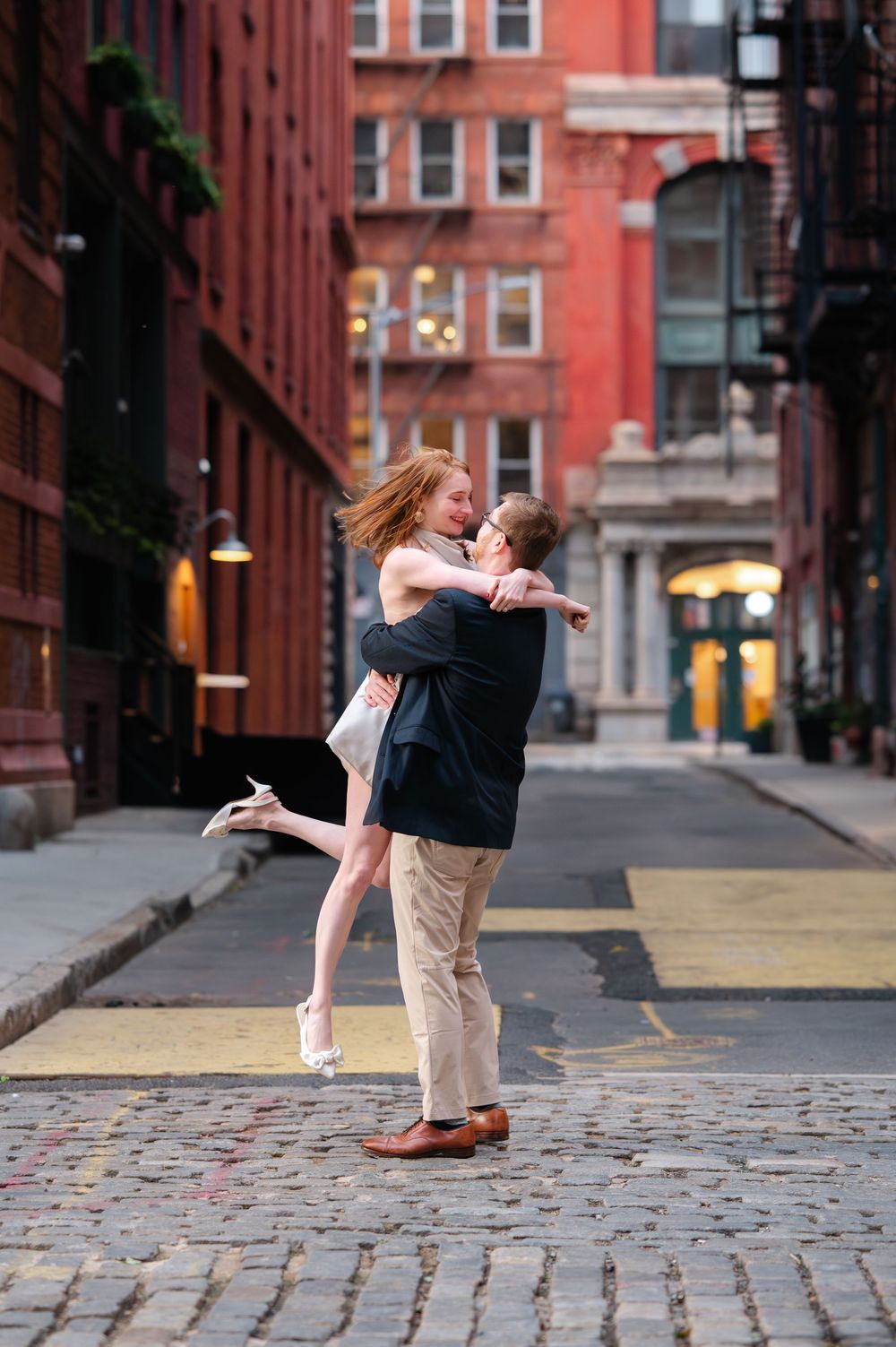 A couple dances romantically on a cobblestone street in front of historic brick buildings in an urban setting.