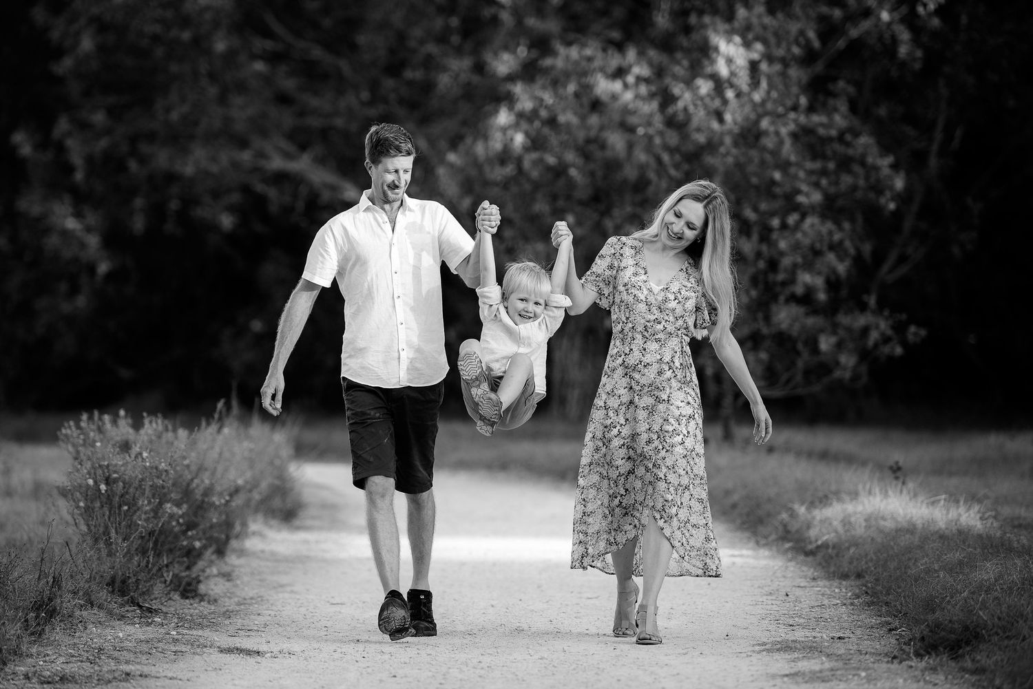 Mother and father walking on a path, holding hands with their toddler and swinging him in the air - Kelly Chapman Photographer Perth