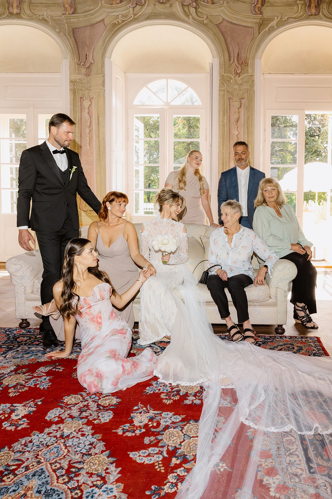 Wedding party gathered in elegant room with ornate decor and red carpet for formal photos.