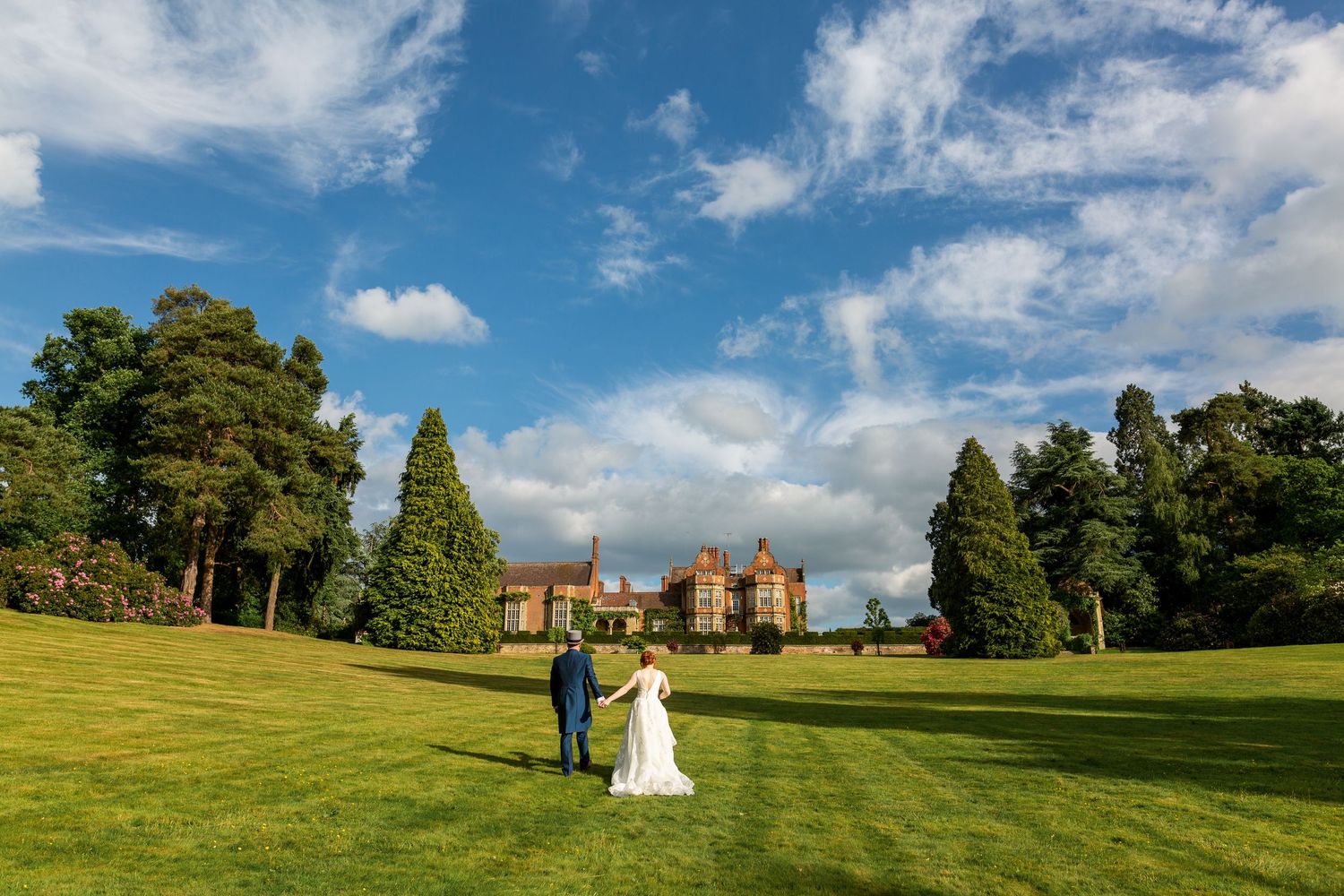 Panoramic view of historic Tudor-style brick buildings with ornate chimneys and landscaped courtyard under blue skies at Tylney Hall