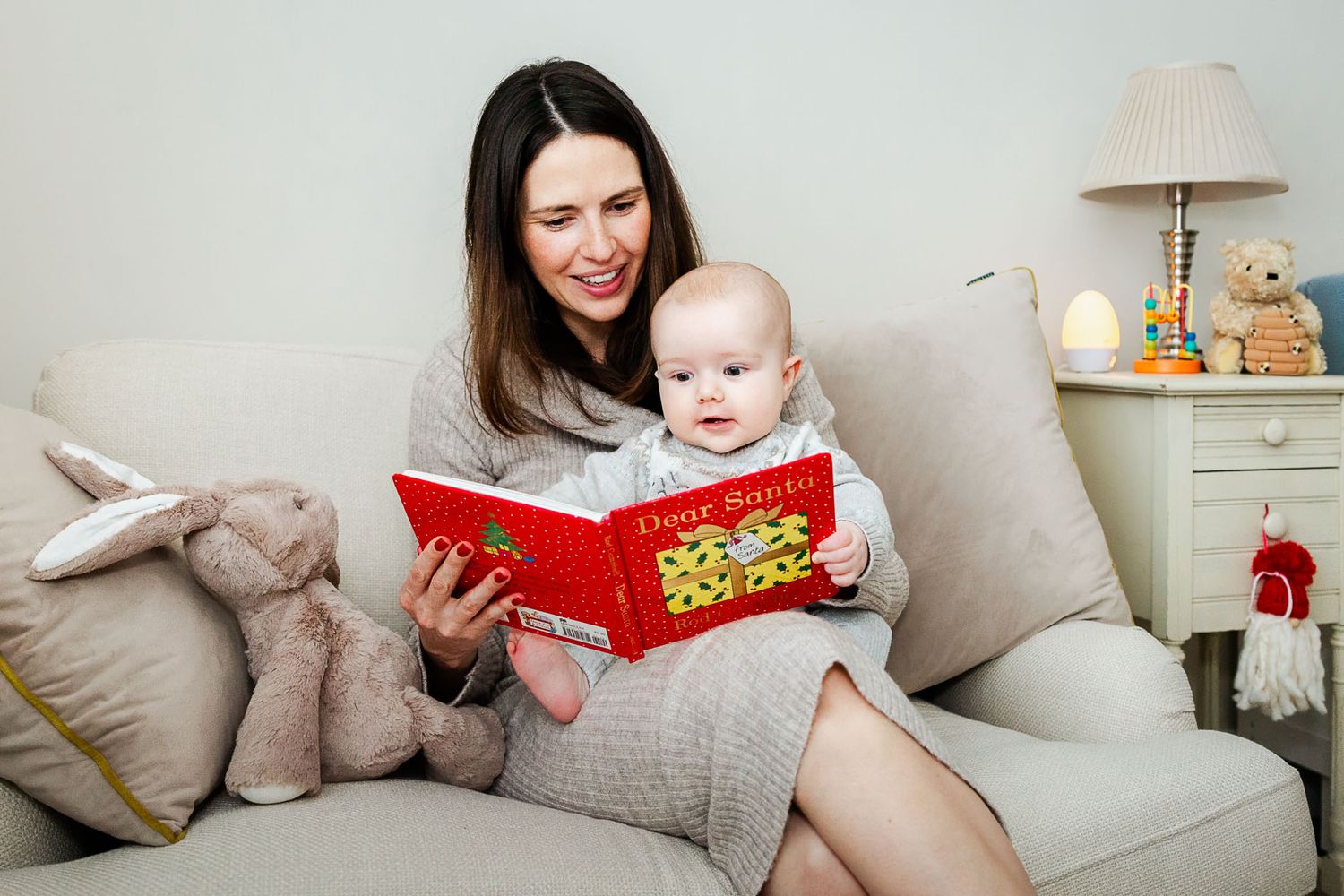 A baby sits on his mum's lap at home and reads the book Dear Santa. They look natural and relaxed at their Bristol Christmas photoshoot