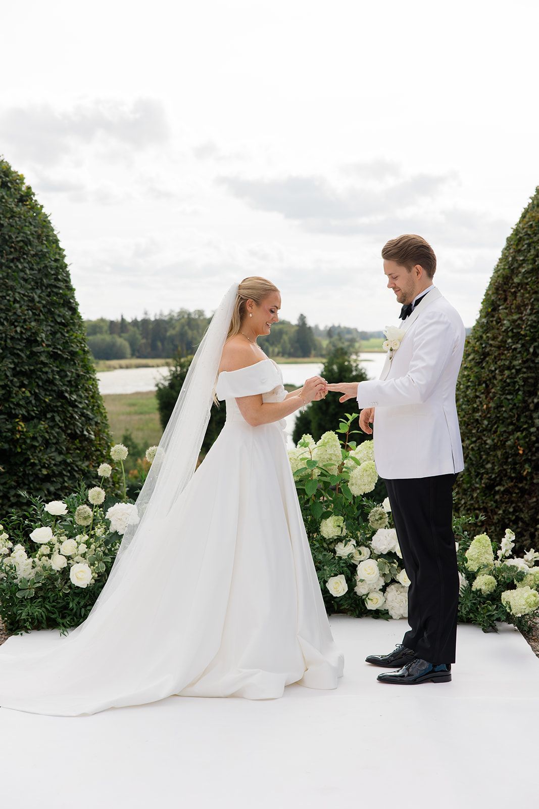 A bride and groom share a playful dance sequence on a white terrace surrounded by manicured hedges and white flowers.
