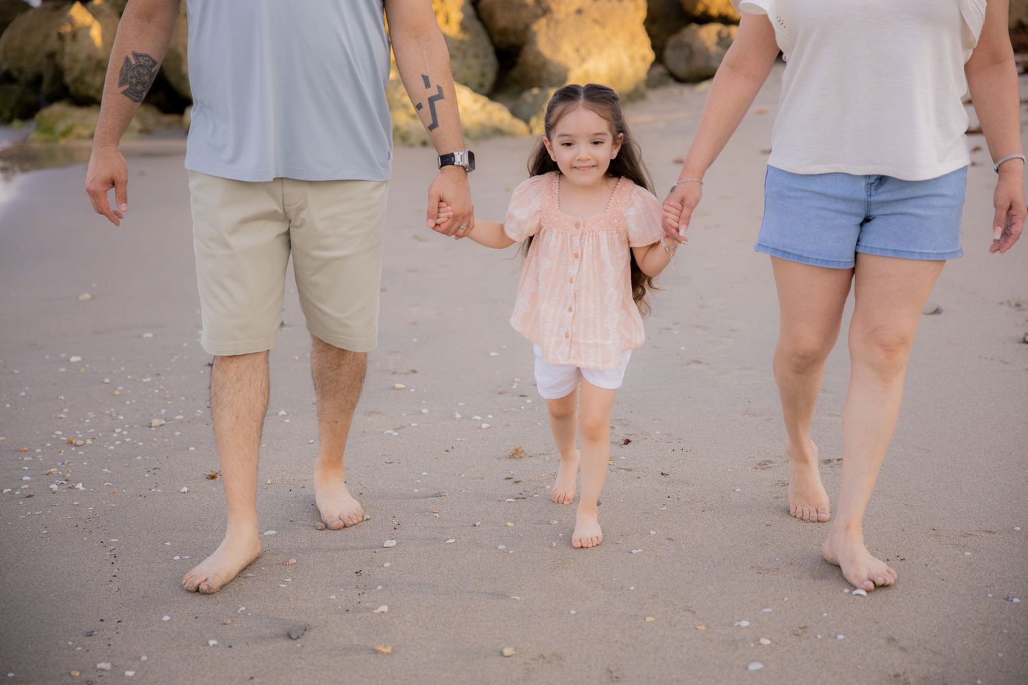 Picture of mom and dad holding hands with faces cropped out showing the daughter in the middle at Deerfield Beach