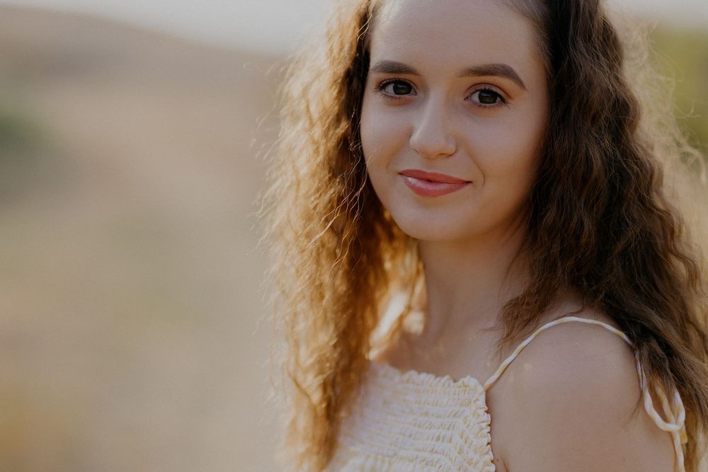 A series of portrait photos showing someone with long dark curly hair in warm golden sunlight outdoors.