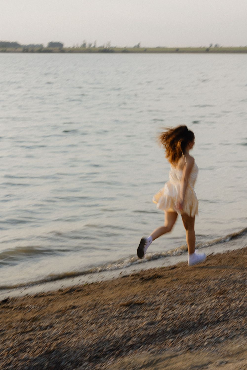 A person in white clothing runs playfully along the water's edge at a rocky beach.