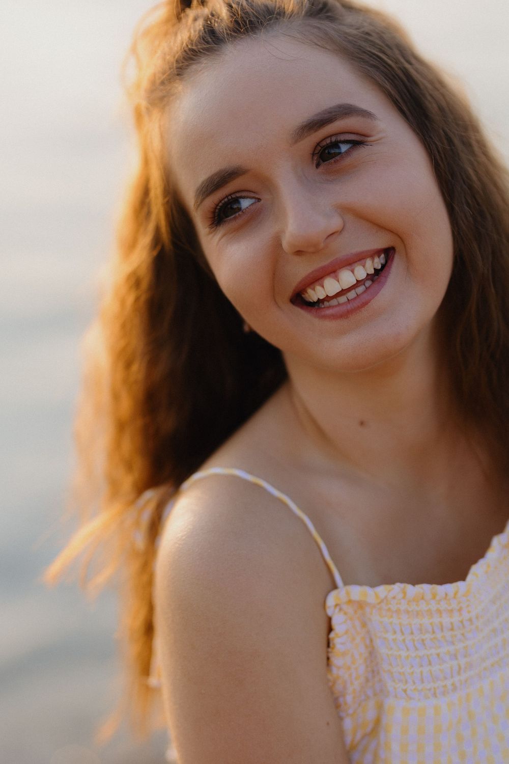 A close-up portrait shows a bright smile against a soft sunset backdrop.