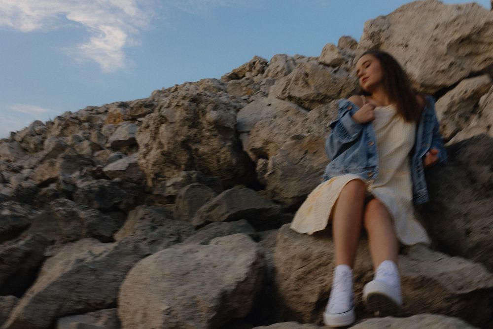 A dreamy lifestyle photo captures someone in denim relaxing on coastal rocks at dusk.