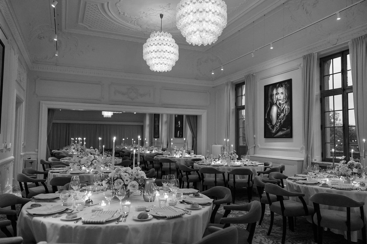Elegant dining room with crystal chandeliers, round tables, and classic white decor in an upscale restaurant setting.