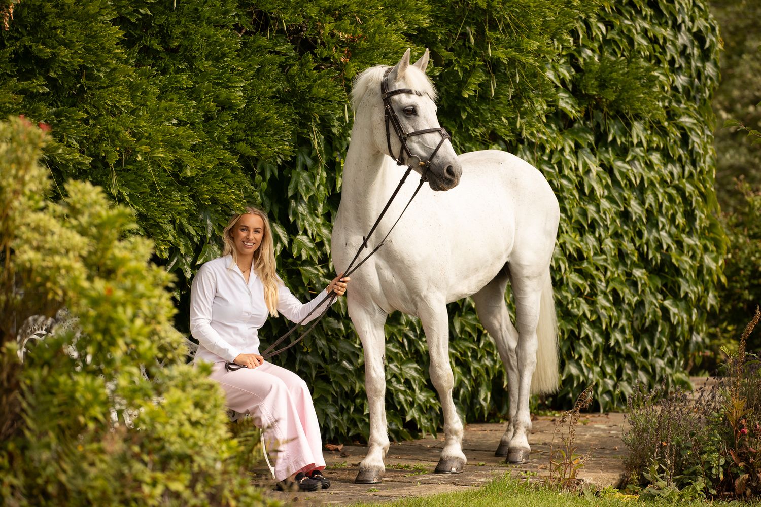 A group poses with horses along a tree-lined path during a sunny autumn day for outdoor photos.
