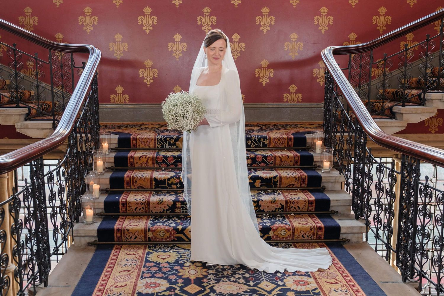 Elegant staircase with ornate railings and red patterned wallpaper in a luxury hotel interior.
