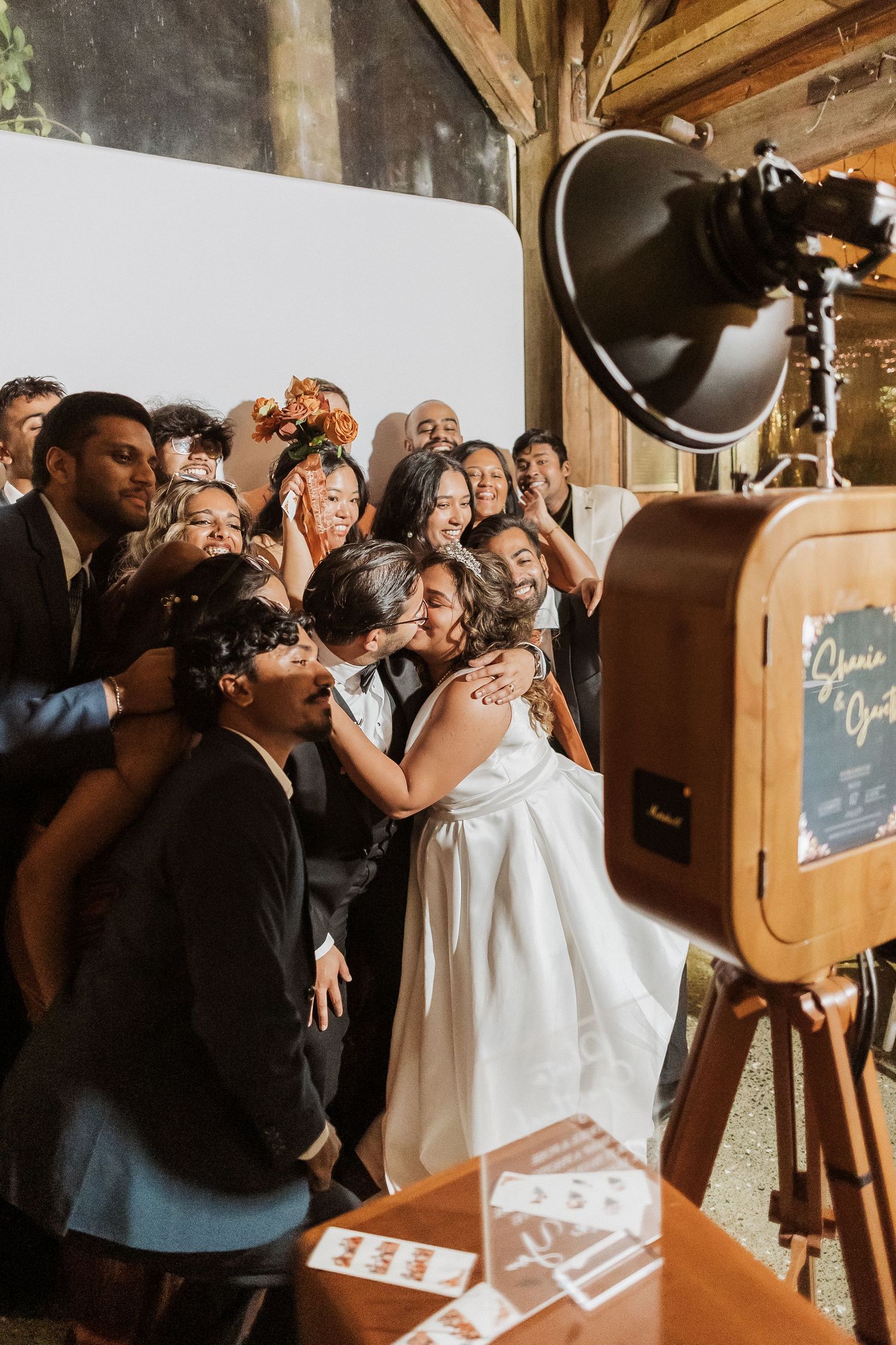 Wedding guests gather around a vintage photo booth to take fun pictures at a rustic reception venue.