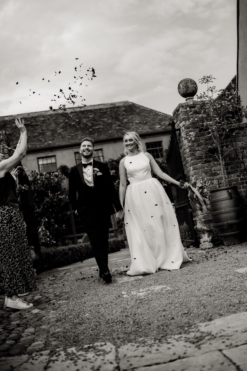 Black and white photo of newlyweds celebrating with guests throwing confetti in a courtyard.