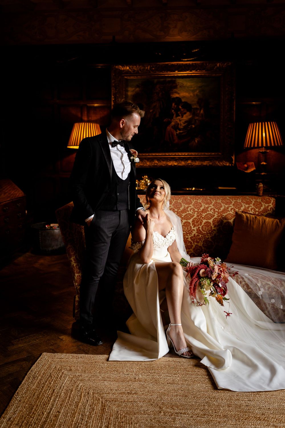 Elegant wedding photo in dimly lit room with vintage furniture and ambient lamp lighting.