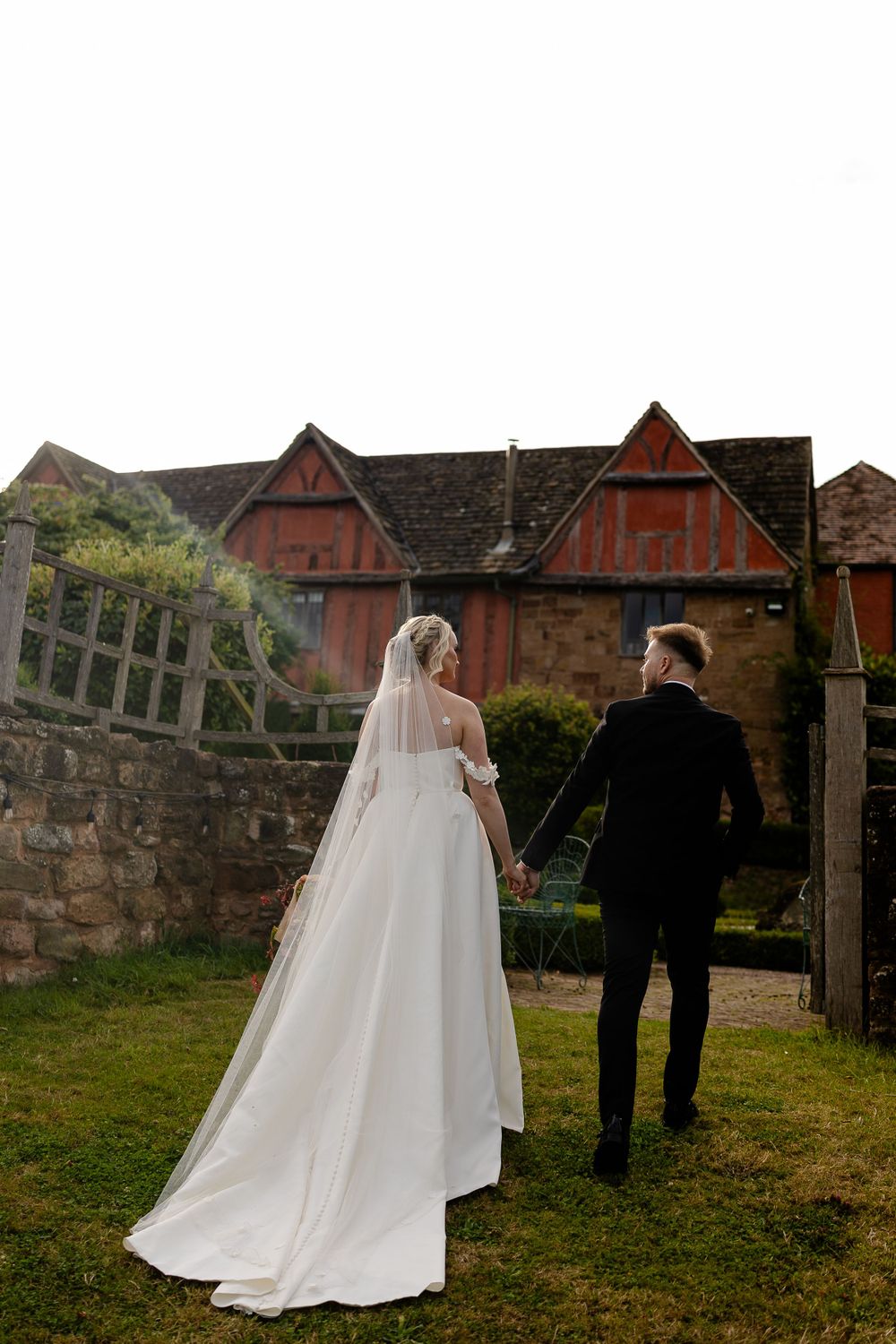 Wedding couple walking towards historic Tudor-style building with red timber framing.