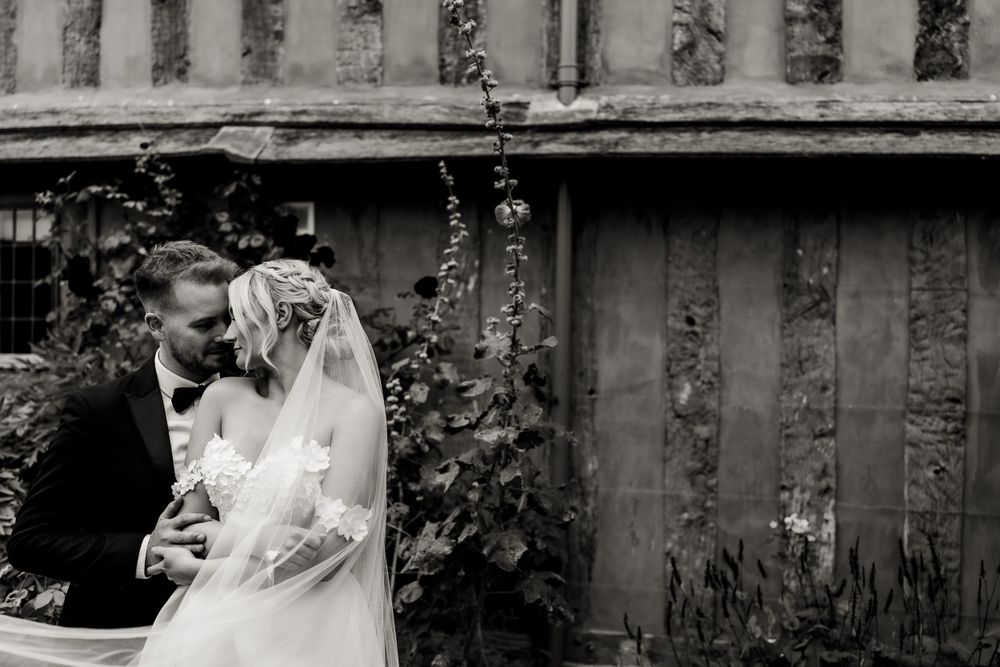 Black and white portrait of newlyweds sharing a tender moment by a vintage building.
