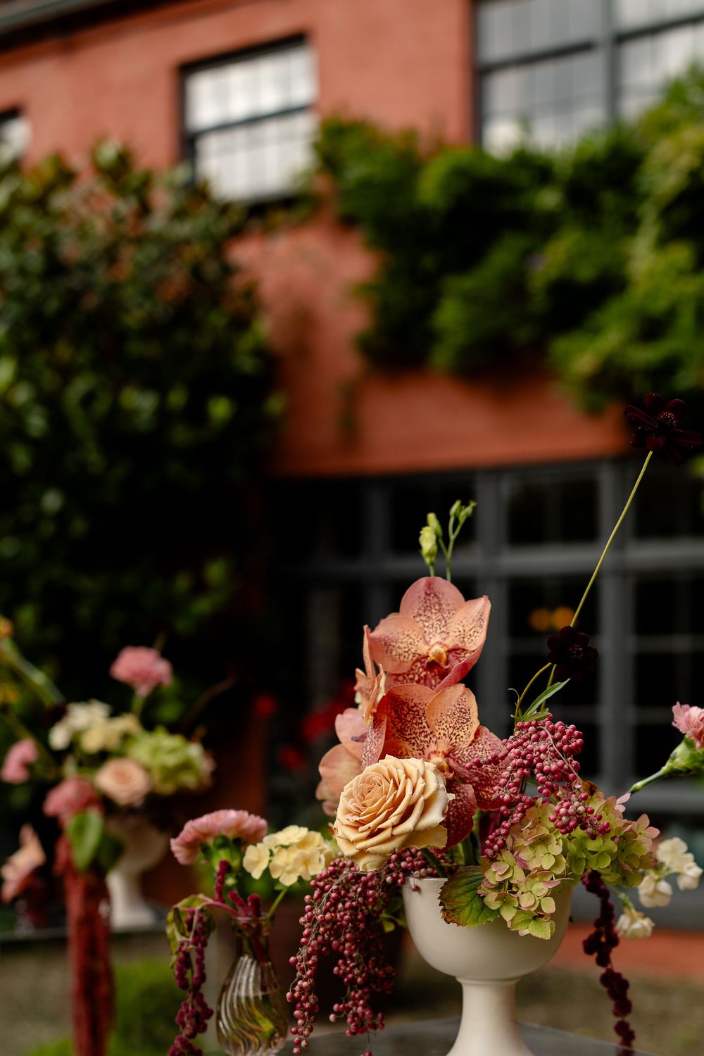 Elegant floral arrangement with pink orchids and roses in a white vase against a coral building.