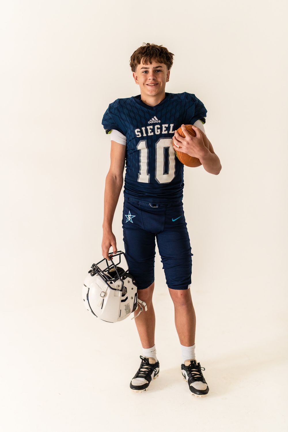 Youth football player in navy blue uniform poses playfully against white backdrop.