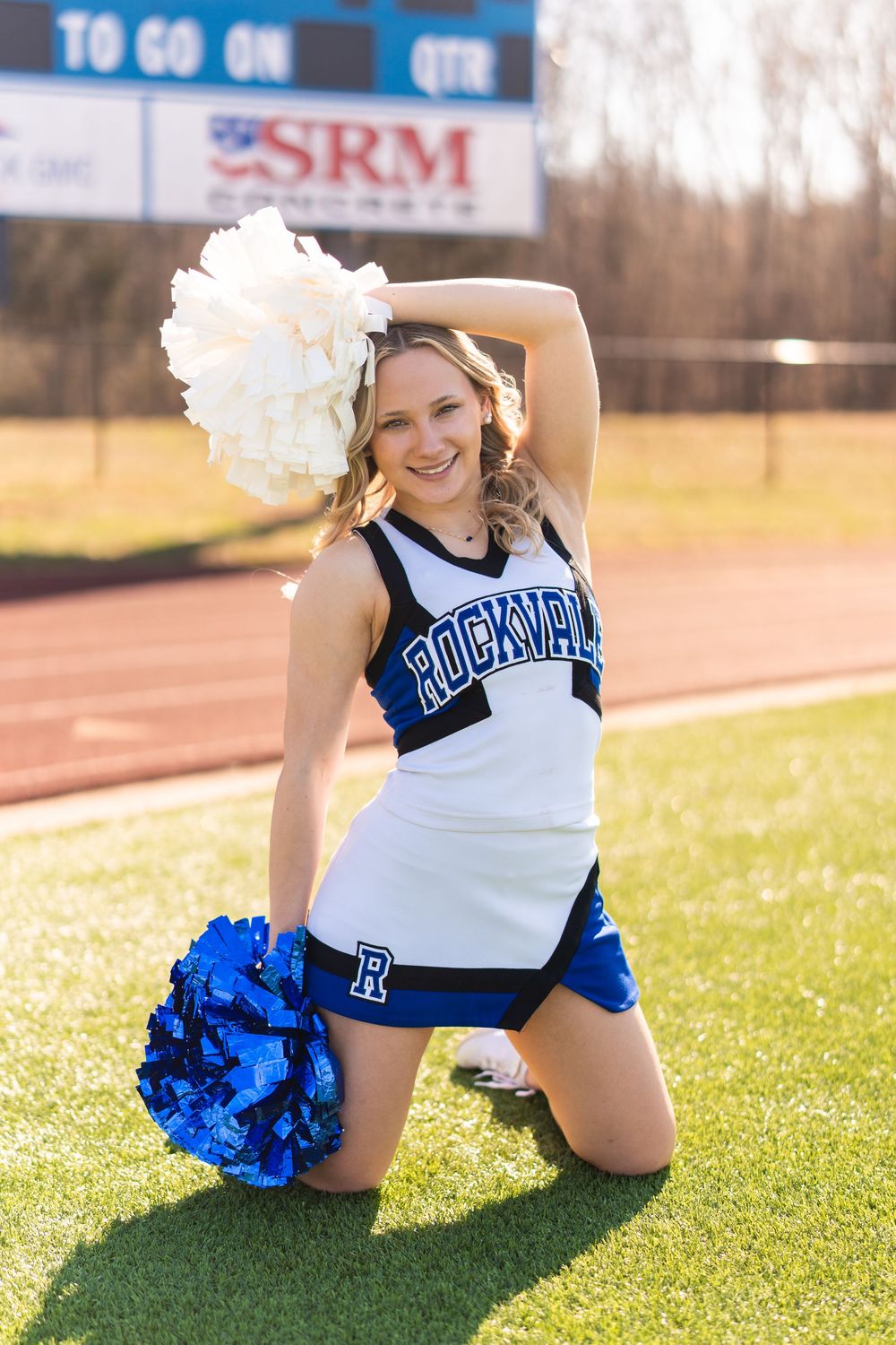Rockvalle cheerleader posing on field with blue and white pom-poms in uniform.