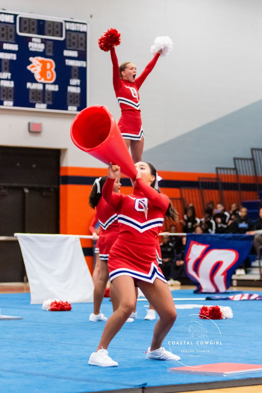 Cheerleader in red and white uniform performs dynamic dance moves on blue competition mat during routine.