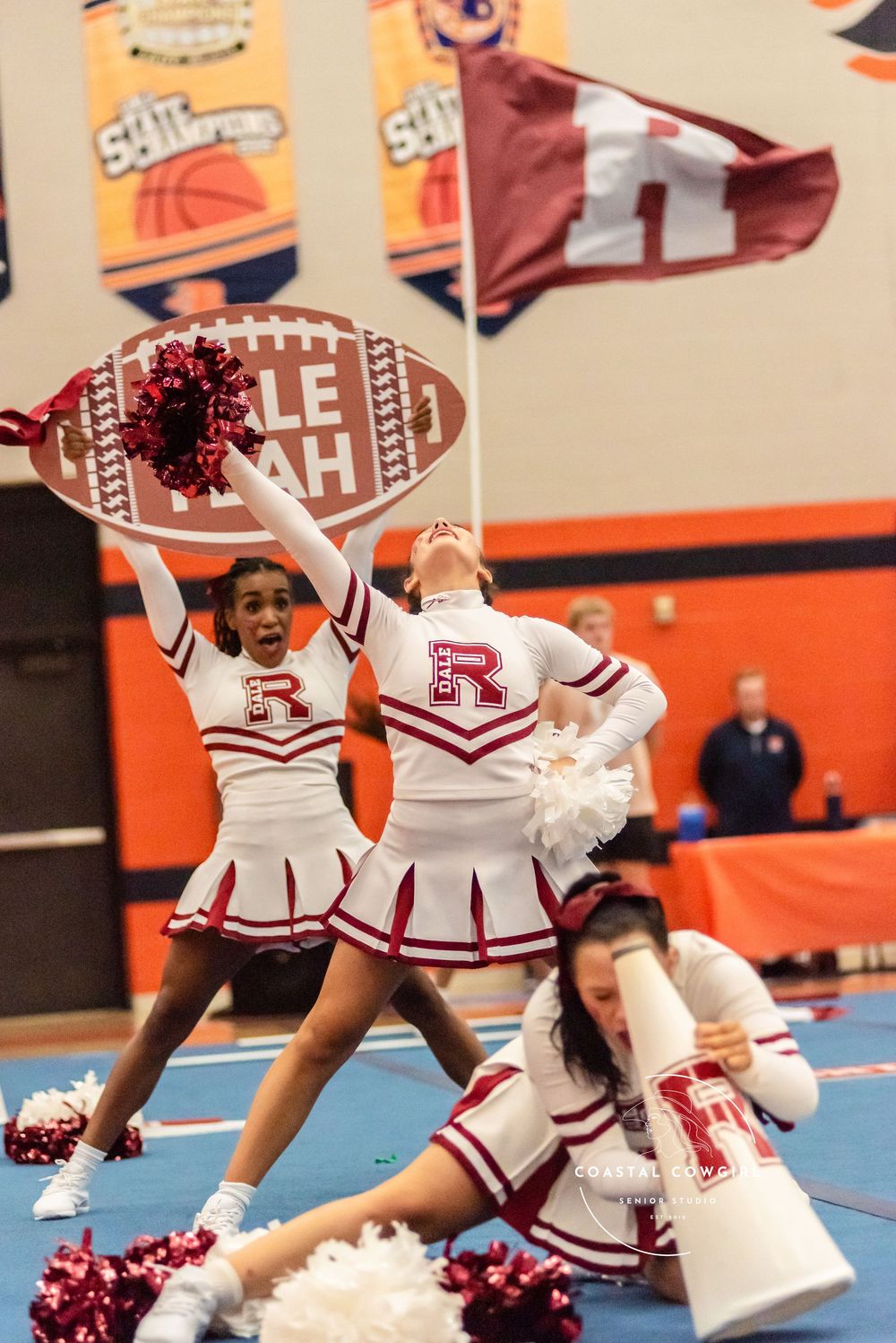 Cheerleaders in white and red uniforms perform synchronized floor routines during a high school sporting event.