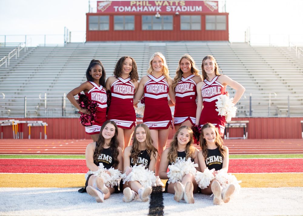 High school cheerleading squad in maroon uniforms poses together on bleachers at Tomahawk Stadium.