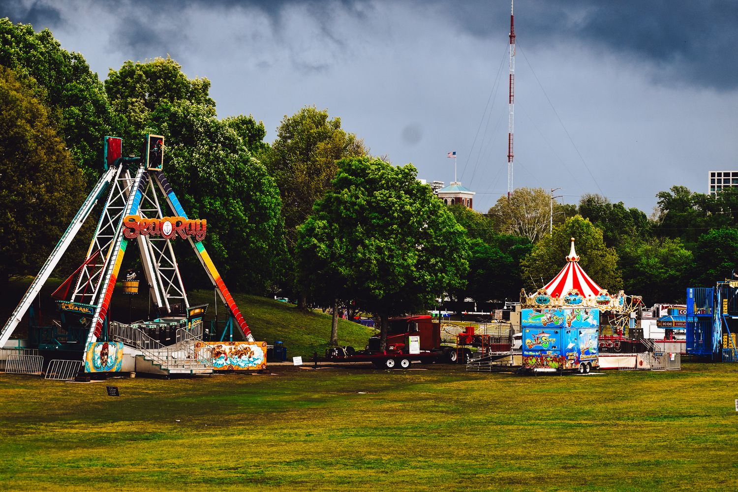 Carnival rides and attractions set up in a park under stormy skies.