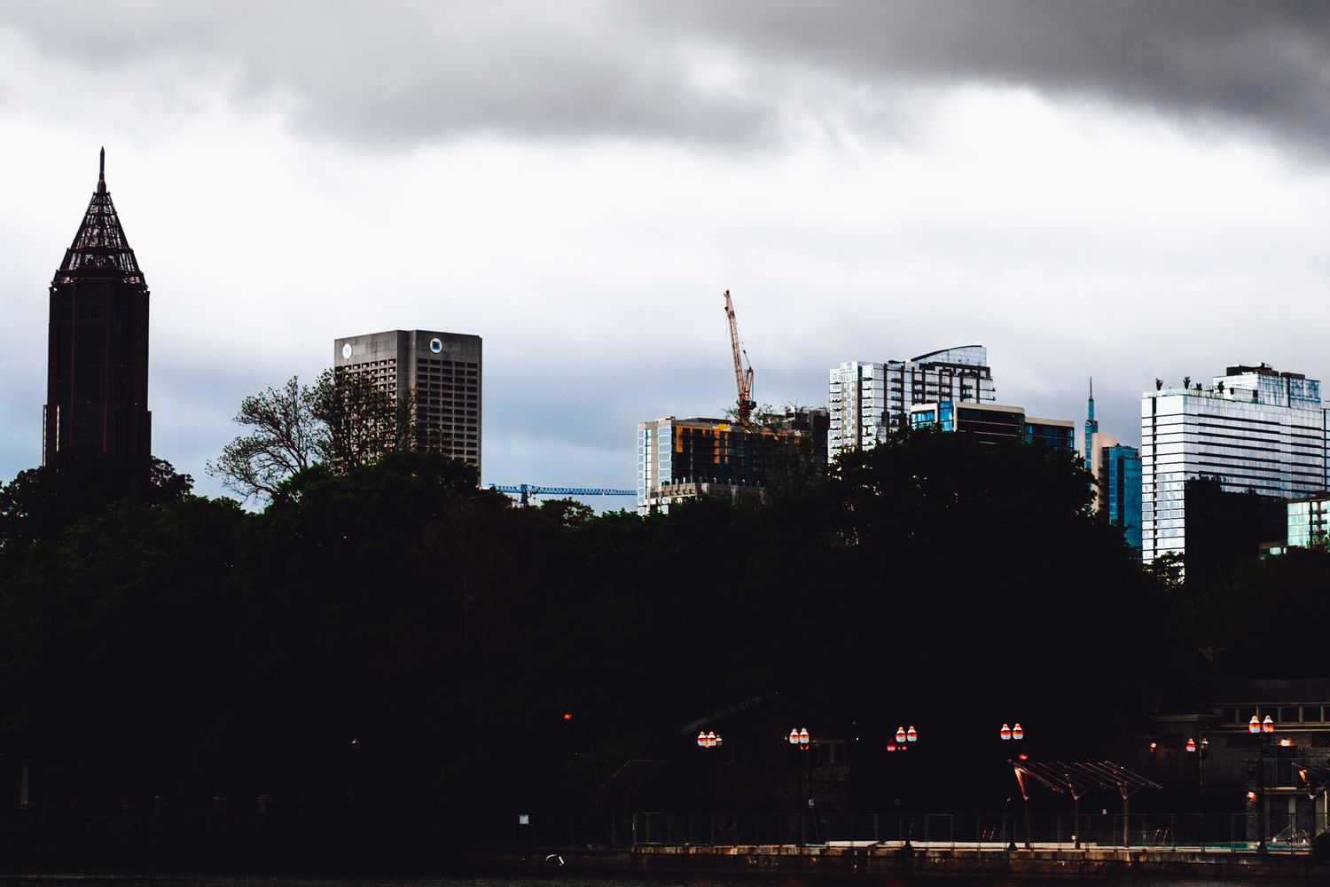 City skyline silhouetted against cloudy sky with buildings and construction cranes visible at dusk.