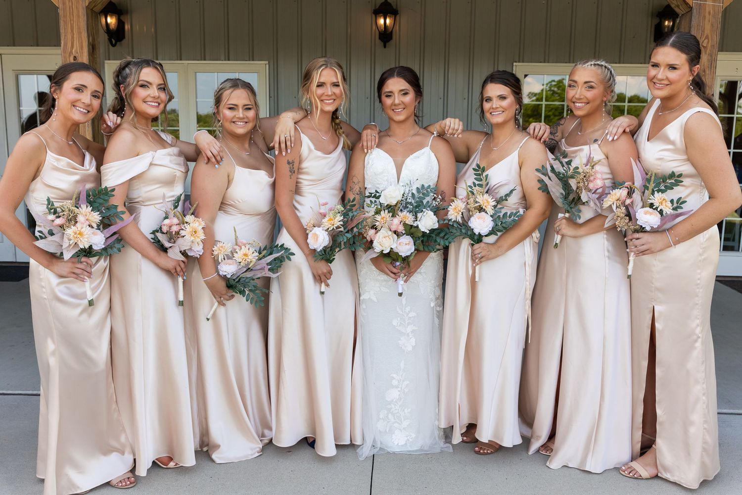 Wedding party in matching champagne-colored dresses posing together outside.