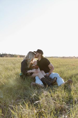 Couple sitting together in golden grass field at sunset with warm sunlight creating romantic atmosphere.