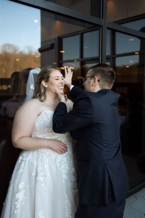 Newlyweds share playful moment against glass windows during wedding photoshoot.