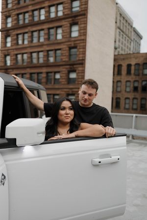 Four photo sequence of a playful couple leaning into a white convertible car against an urban backdrop.
