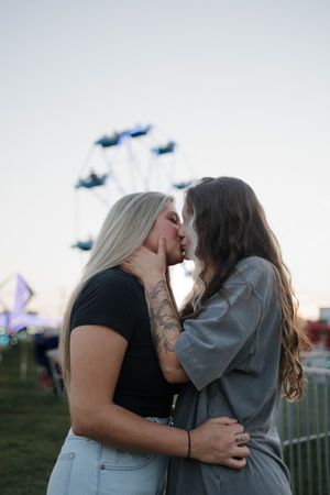 A romantic embrace at sunset with carnival rides visible in the background at an outdoor festival.